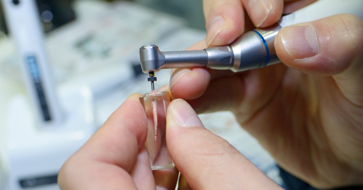 A pair of hands holding a plugger and using it to inject a light pink filling into a clear, rectangular mold.
