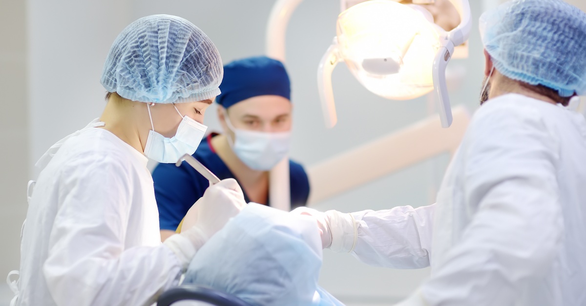 A dental team performing a procedure on a patient lying under surgical lights in a clinical operating room.