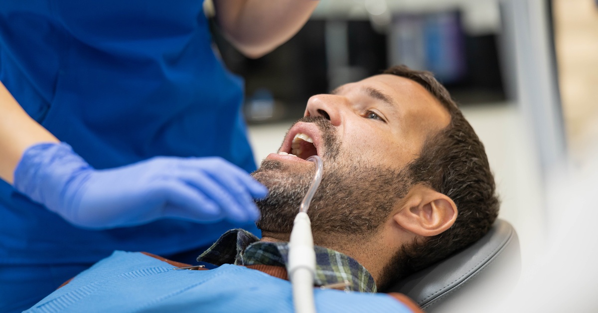 A patient reclining in a dentist chair while a dental professional performs a procedure in a bright modern clinic.