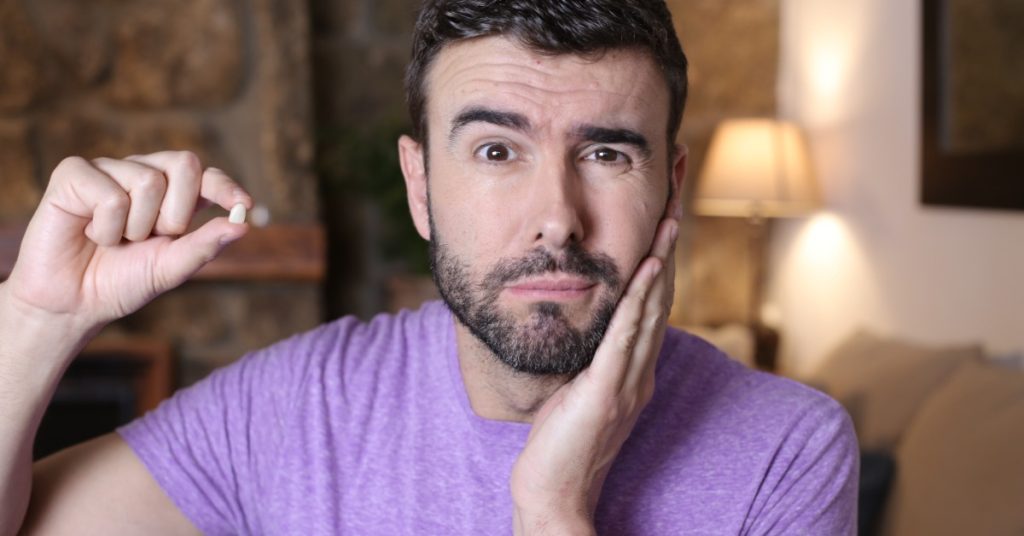 A young man holding a loose tooth between his fingers near his mouth while looking forward with a neutral expression.