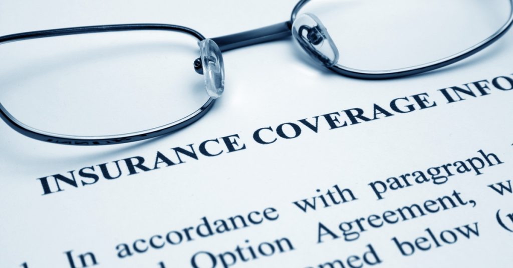 A close-up of an insurance coverage document with black eyeglasses resting over printed policy text.