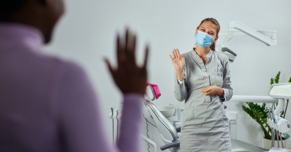 A patient waving goodbye to a dental professional while leaving a modern office after an appointment.